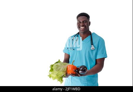 Ein lächelnder afroamerikanischer Arzt hält frisches Gemüse in den Händen auf einem isolierten weißen Hintergrund. Stockfoto
