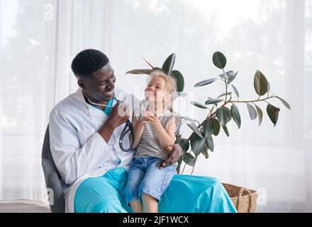 Ein afroamerikanischer Arzt kommuniziert mit einem kleinen Mädchen, das auf dem Schoß des Arztes sitzt Stockfoto