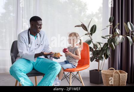 Ein afroamerikanischer Ernährungsberater erzählt einem kleinen Patienten von einer richtigen und gesunden Ernährung. Stockfoto