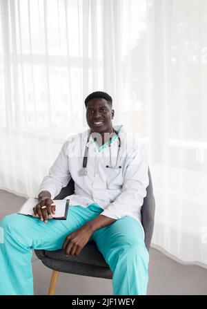 Porträt eines afrikanischen Arztes, der lächelnd auf einem Stuhl sitzt Stockfoto