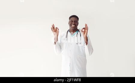 Der afroamerikanische Arzt zeigt sich in Ordnung. Ein Mann im weißen Mantel sagt, dass alles in Ordnung ist. Studio-Foto Stockfoto