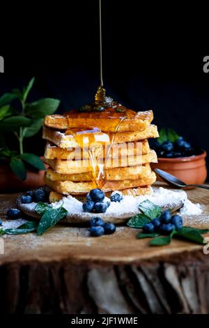 Honig gießt auf Waffeln mit frischen Heidelbeeren auf dem rustikalen Tisch. Frisch gebackene belgische Waffeln Stockfoto