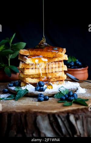 Honig gießt auf Waffeln mit frischen Heidelbeeren auf dem rustikalen Tisch. Frisch gebackene belgische Waffeln Stockfoto