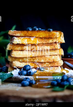 Waffeln mit frischen Heidelbeeren und Honig auf dem rustikalen Tisch. Frisch gebackene belgische Waffeln Stockfoto