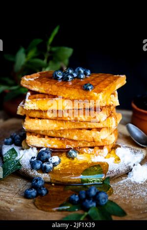 Waffeln mit frischen Heidelbeeren und Honig auf dem rustikalen Tisch. Frisch gebackene belgische Waffeln Stockfoto
