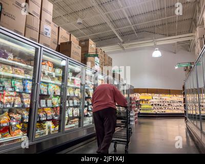 Mill Creek, WA USA - ca. Mai 2022: Abgewinkelte Ansicht einer älteren Frau in einem pinken Hoodie, die im Tiefkühlbereich eines Stadt- und Landmarktes einkaufen geht. Stockfoto