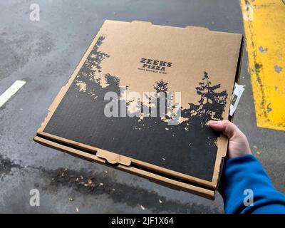 Seattle, WA USA - ca. Mai 2022: Nahaufnahme von jemandem, der eine Zeeks Pizzakiste auf einem Parkplatz hält. Stockfoto