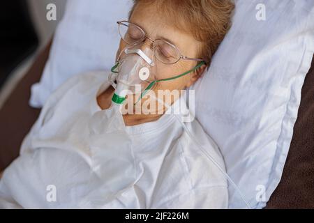 Die ältere Patientin in einer Atemmaske liegt während der Behandlung von Covid-19 auf der Station Stockfoto