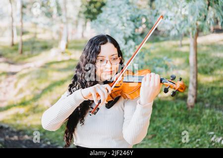 Lockige Brünette Frau mit Brille spielt Geige im Wald. Selektiver Fokus. Stockfoto