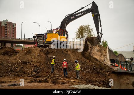 Ein Bagger zerstört eine Autobahnrampe und legt Schmutz in einen Muldenkipper. Stockfoto