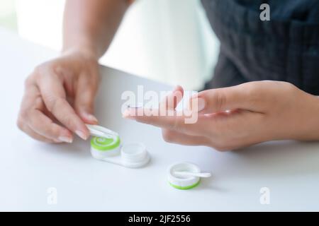 Frau legt es unten Kontaktlinse auf ihren Zeigefinger mit einer Pinzette. In der Nähe befindet sich ein Behälter für Linsen. Nahaufnahme, Seitenansicht Stockfoto