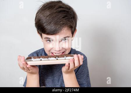 Der 9-jährige Junge zeigt seine Zähne und hält ein Tablett mit mehreren brasilianischen Fudge-Bällen. Stockfoto