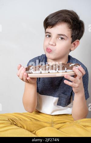 Das 9-jährige Kind hält ein Tablett mit mehreren brasilianischen Fudge-Bällen und puckert ihre Lippen. Stockfoto