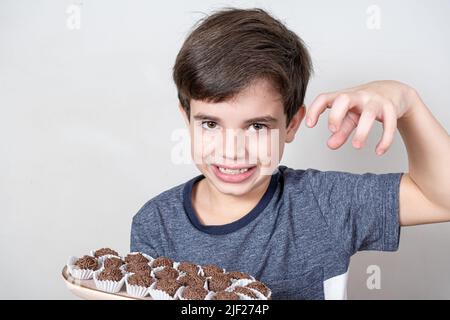 9-Jähriger hält ein Tablett mit mehreren brasilianischen Fudge-Kugeln, bereit, sie zu fangen. Stockfoto