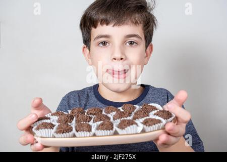 Der 9-jährige Brasilianer hält ein Tablett mit mehreren brasilianischen Fudge-Bällen und leckt seine Lippen. Stockfoto