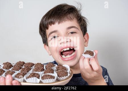 Der 9-jährige Brasilianer hält ein Tablett mit mehreren brasilianischen Fudge-Bällen und mit offenem Mund. Stockfoto