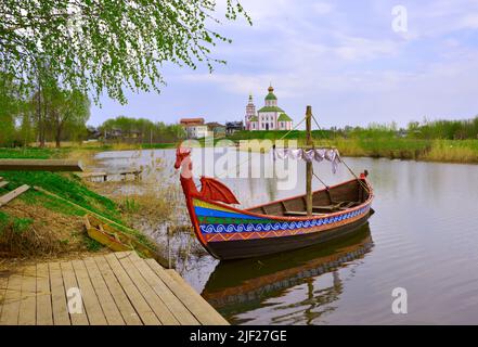 Touristenboot am Pier. Drakkar auf dem Fluss, Elijah Kirche am Horizont, Architektur des XVIII Jahrhunderts. Susdal, Russland, 2022 Stockfoto