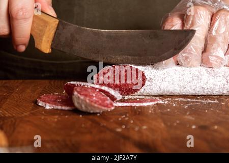 Verkäuferin schneidet Salami-Wurst auf Holzbrett. Stockfoto