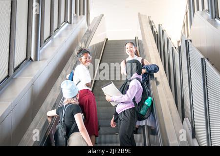 Eine Gruppe glücklicher junger Studentinnen, die die Rolltreppe hochgehen. Zurück zum College-Konzept. Stockfoto