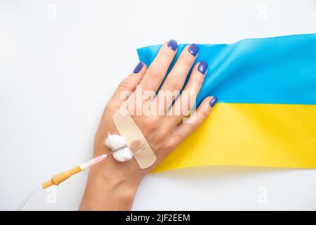 Die Hand einer Frau mit einem Dropper und die Flagge der Ukraine auf weißem Hintergrund, der Krieg in der Ukraine, Zivilisten werden im Krieg getötet Stockfoto