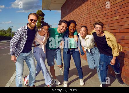 Unbeschwerte internationale Gruppe von Freunden in lässigen Outfits lächeln und umarmen auf der Straße. Stockfoto