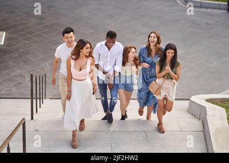 Gruppe von multirassischen Freunden, die lachen und plaudern, während sie die Treppe im Freien hinaufgehen. Freunde, die Armbänder mit LGBT-Flagge tragen. Vielfalt, Freundschaft und LGBT-Konzept. Stockfoto