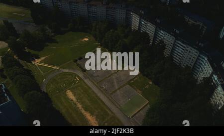 Ein altes Schulstadion in einem Stadtblock. Gesprungener Asphalt und Sportgeräte. Mehrstöckige Gebäude und eine große Grünfläche. Luftaufnahmen. Stockfoto