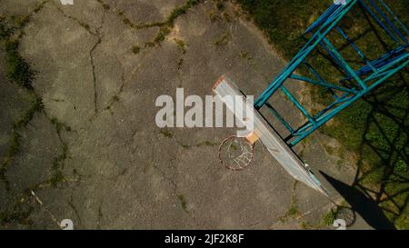 Altes Basketball-Backboard. Aus Brettern. Abblätternde Farbe und ein beschädigter Korb. Auf dem Gelände befindet sich ein alter gesprungener Asphalt. Von oben aufgenommen. Antenne Stockfoto
