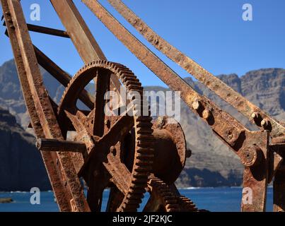 Alter rostiger Kran im Vordergrund und Berge im Hintergrund, altes Dock von Agaete, nördlich von Gran Canaria, Kanarische Inseln Stockfoto