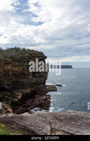 Eine Vertikale einer felsigen Klippe mit viel Grün vor einem blauen Meer bedeckt Stockfoto