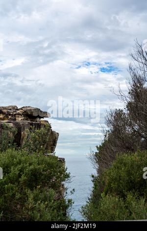 Eine Vertikale einer felsigen Klippe mit viel Grün vor einem blauen Meer bedeckt Stockfoto