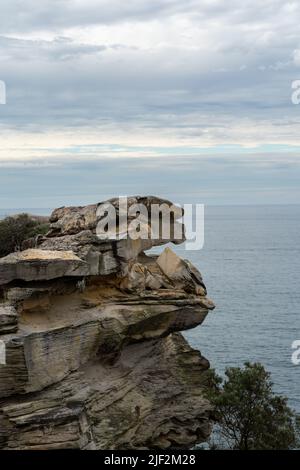 Eine Vertikale einer felsigen Klippe mit viel Grün vor einem blauen Meer bedeckt Stockfoto