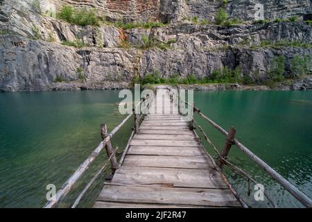 Hölzerne Brücke, die von Filmemachern in einem überfluteten Kalksteinbruch „Velká Amerika“ im tschechischen Karst gebaut wurde, der zu einer Klippenküste am Boden der Grube führte. Stockfoto