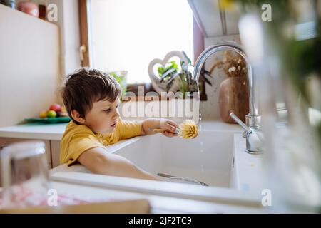 Kleiner Junge Waschbecher im Waschbecken in der Küche mit Holzpeeling, nachhaltige Lebenslaus. Stockfoto
