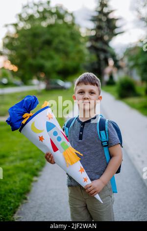 Kleiner Junge mit Schultasche am ersten Schultag, hält Schulkegel mit Geschenken Stockfoto