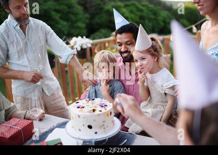 Eine Familie mit mehreren Generationen feiert Geburtstag und hat eine Gartenparty draußen im Hinterhof auf der Terrasse. Stockfoto