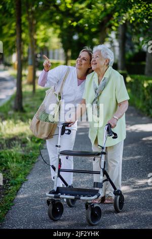 Pfleger mit älterer Frau auf Spaziergang mit Wanderer im Park mit Einkaufstasche. Stockfoto