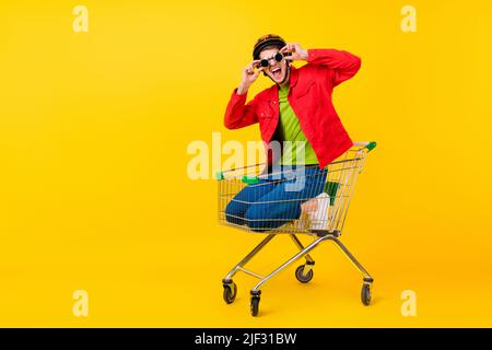 Ganzkörper-Foto von cool Millennial Brunet Kerl gehen in Trolley tragen Jacke Hose Sneaker isoliert auf gelbem Hintergrund Stockfoto