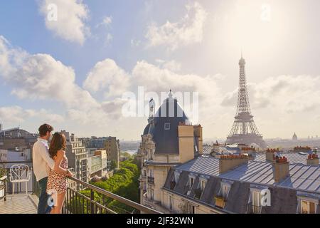 Aufnahme eines jungen Paares, das den Blick vom Balkon einer Wohnung mit Blick auf den Eiffelturm in Paris, Frankreich, bewundert Stockfoto