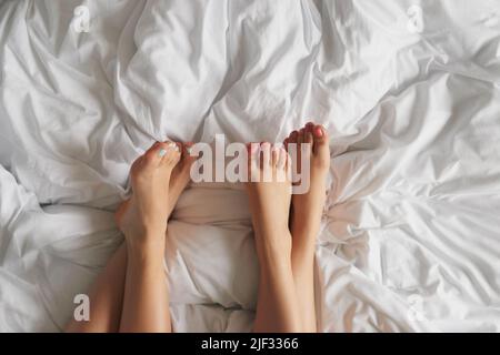 Zwei unverkennbare Füße von Frauen, die sich zu Hause auf dem Bett entspannen, im Hochwinkelshot Stockfoto