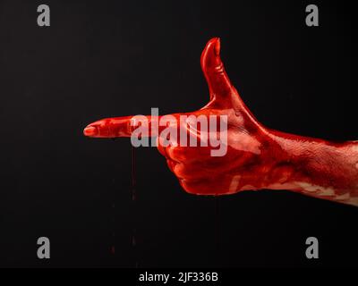 Die blutige Hand einer Frau zeigt eine Geste einer Waffe auf schwarzem Hintergrund. Stockfoto