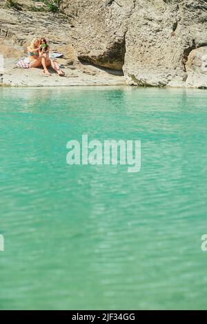 Glückliche Freunde im Urlaub, die Selfies auf einem Handy am See machen. Zwei Frauen im Urlaub, die Bikinis tragen, haben vorher Selfies auf einem Handy gemacht Stockfoto