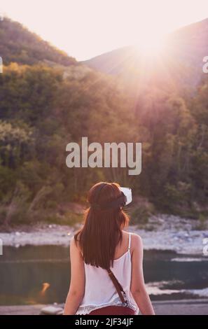 Frau, die eine AR-Brille verwendet, um die Aussicht auf die Berge zu betrachten. Frau im Urlaub mit AR-Googles im Urlaub in den Bergen. Frau, die mit AR spielt Stockfoto