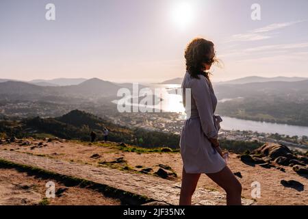 Junge Frau auf einem Berg gegen eine Landschaft mit einem Fluss und Bergen Stockfoto