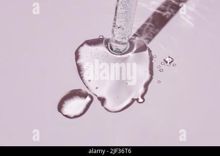 Aus einer Pipette fließt ein kosmetisches Gel oder Kollagenserum mit Blasen auf rosa Hintergrund Stockfoto