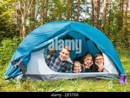 Kinder liegen im Zelt auf einer sonnigen Wiese und genießen sommerlichen Waldcampen. Konzept für Sommerferien mit der Familie Stockfoto