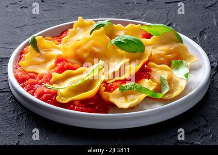 Ravioli mit Tomatensauce und frischen Basilikumblättern auf einem Teller, italienische Pasta-Gericht, auf dunklem Hintergrund Stockfoto