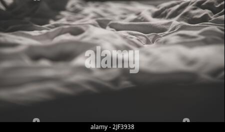 Weiße, zerknitterte, fabulierte Textur, gewellte Oberfläche, Nahaufnahme eines ungefertigten Bettlaschs im Schlafzimmer nach dem Schlafengehen Weiches Scharfstellen. Stockfoto