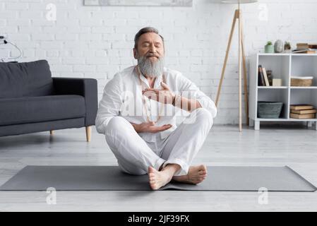 Senior Master Guru meditiert zu Hause in lockeren Posen auf einer Yogamatte Stockfoto