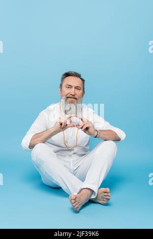 Leitender Guru-Tutor, der mit blauen Beinen gekreuzte Beine zeigt und eine Hakini-Mudra zeigt Stockfoto